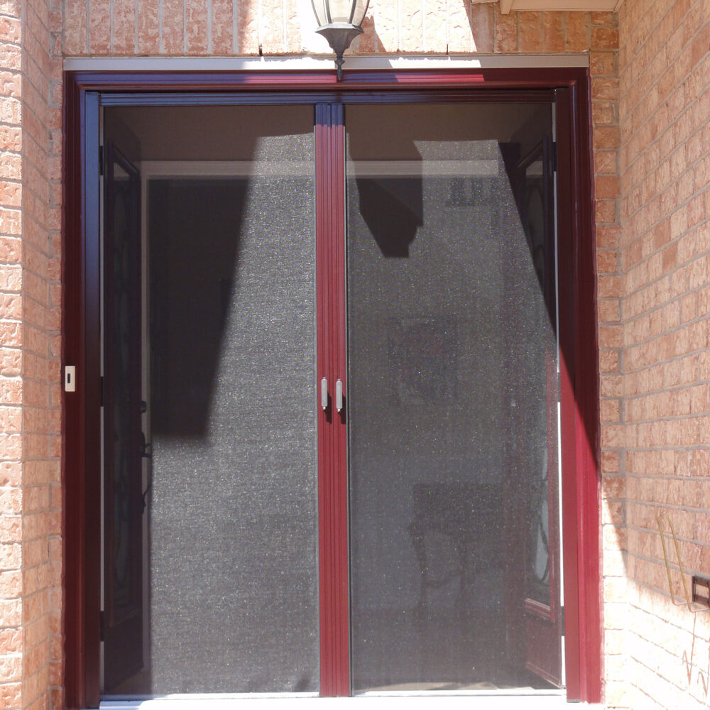 Double black mesh doors with red frames on a brick wall.