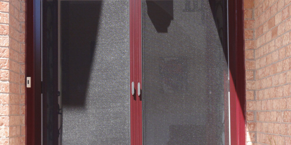 Double black mesh doors with red frames on a brick wall.