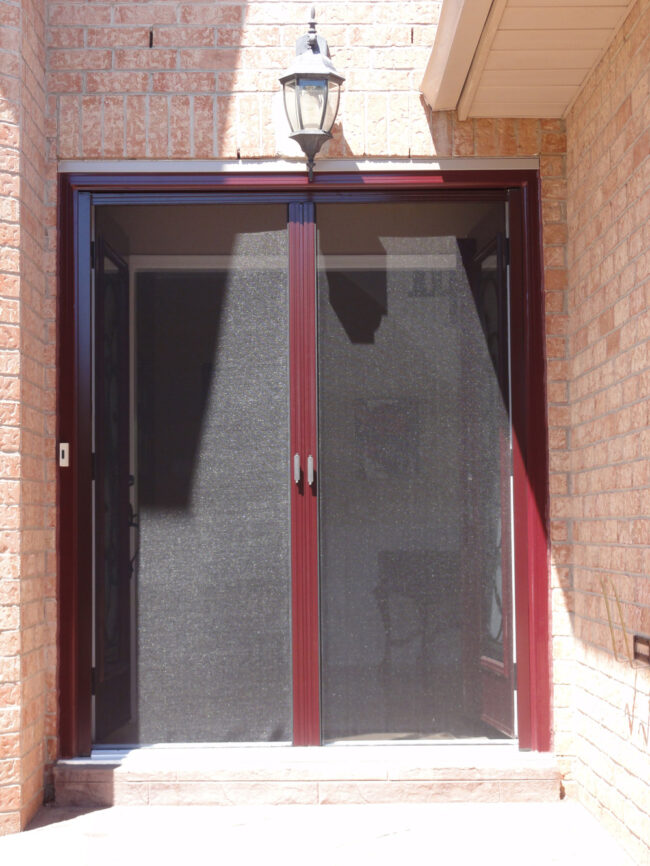 Double black mesh doors with red frames on a brick wall.