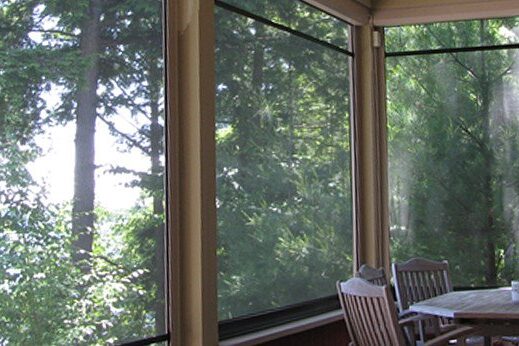 Sunlit room with large windows overlooking green trees.