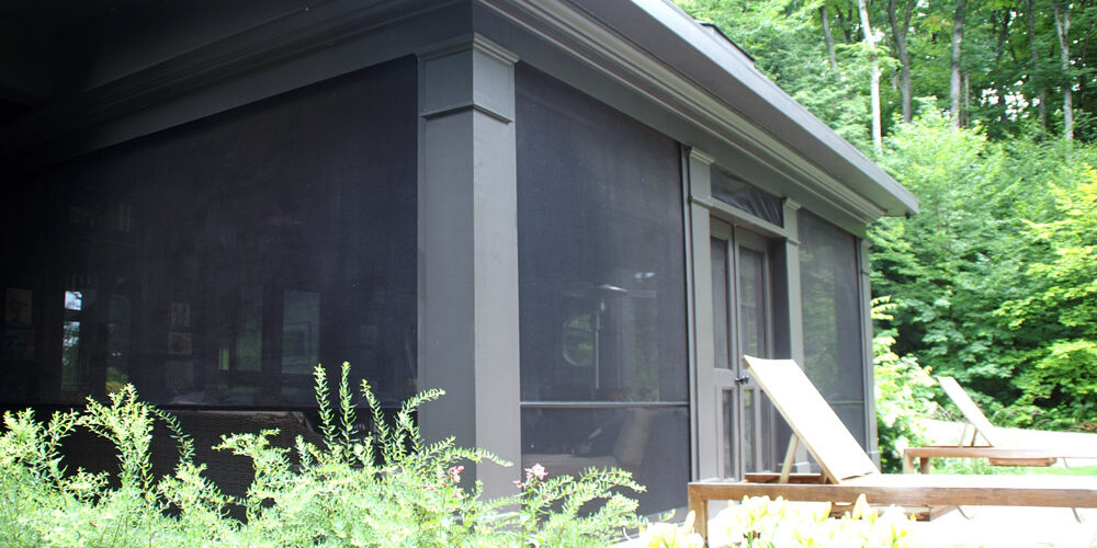 A screened porch attached to a house with outdoor chairs nearby.