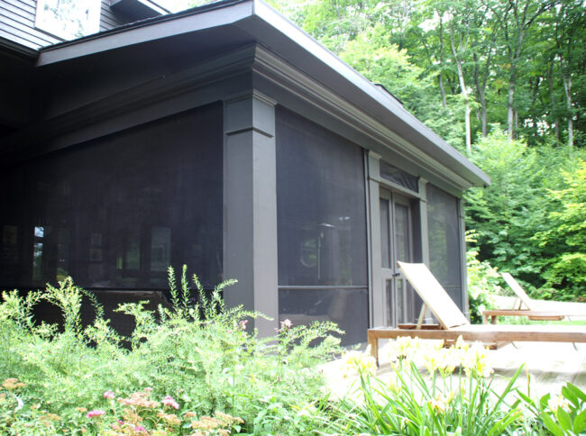 A screened porch attached to a house with outdoor chairs nearby.
