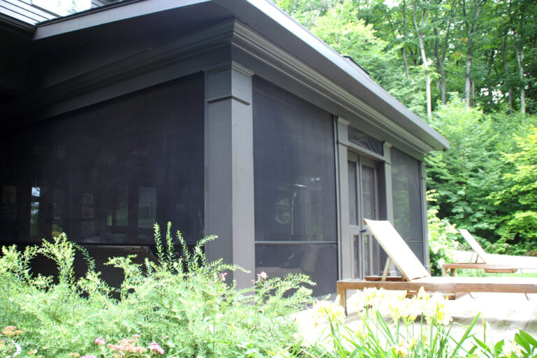 A screened porch attached to a house with outdoor chairs nearby.