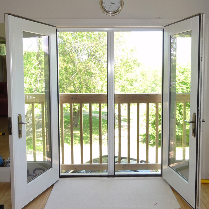 Open double doors leading to a balcony with a green view.