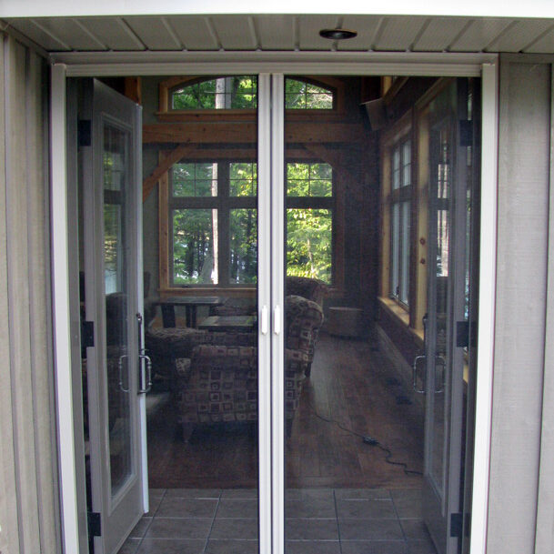 Open double doors leading to a sunlit porch with wooden floors and greenery outside.
