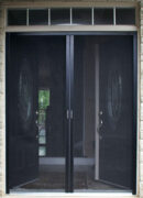 Black sliding mesh door with handles in a doorway.