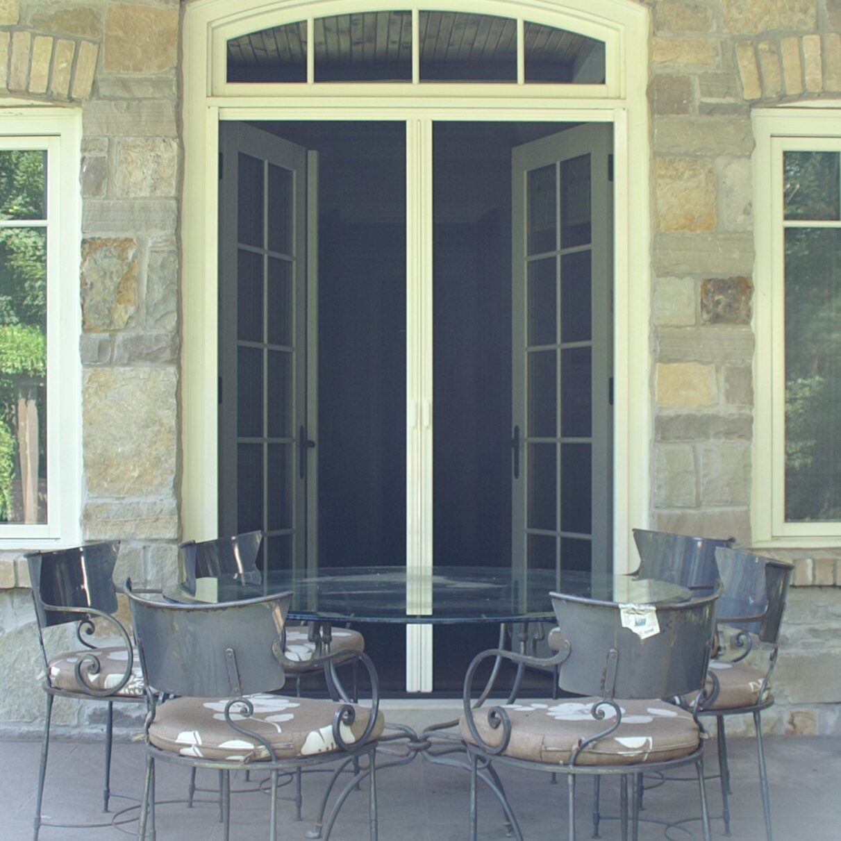 Cozy outdoor patio with a round metal table and four chairs set against a stone wall and glass door.