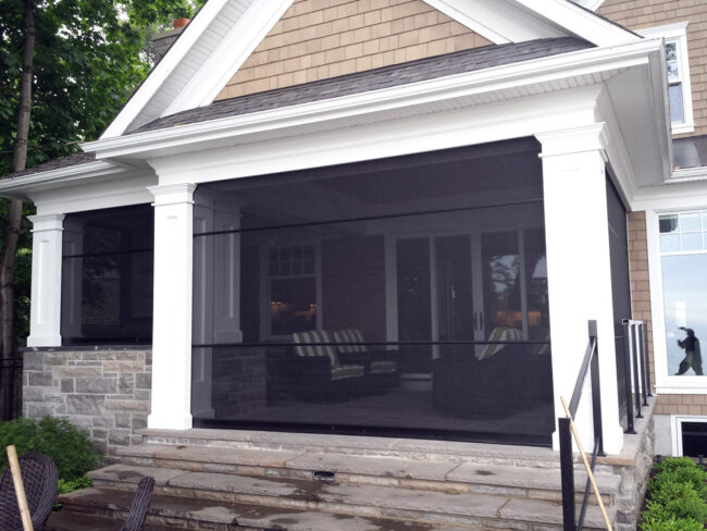 A screened-in porch attached to a house with white pillars and seating inside.
