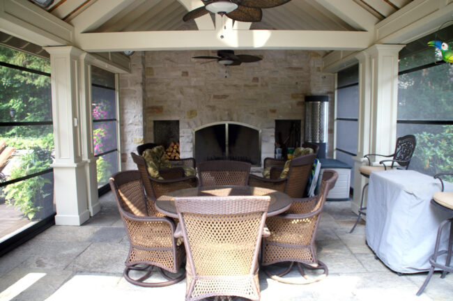 Cozy outdoor patio with wicker chairs and a stone fireplace.