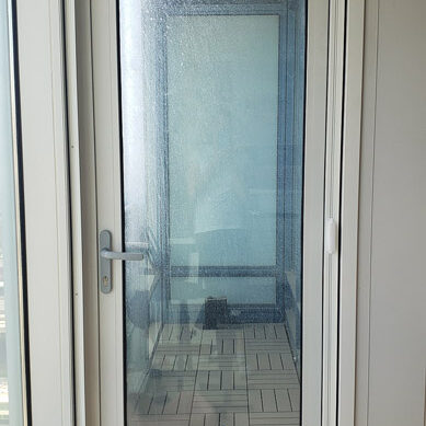 Glass door with a reflection of a patio and furniture outside.