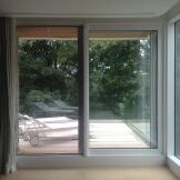 A modern glass sliding door opens to a serene outdoor deck surrounded by greenery.