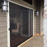 Screen door on a porch with a cushioned chair inside.