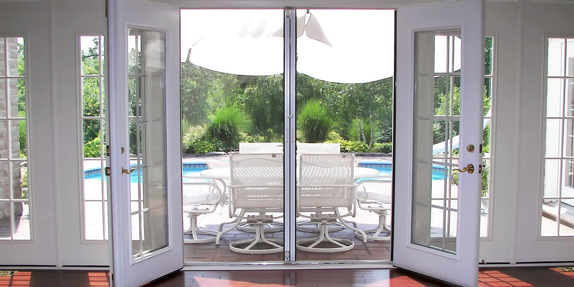 Open French doors reveal a sunny patio with a pool and outdoor seating.