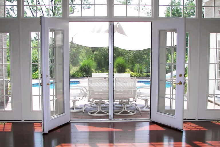 Open French doors reveal a sunny patio with a pool and outdoor seating.